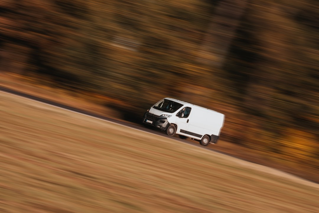 A white delivery van drives quickly down a road.
