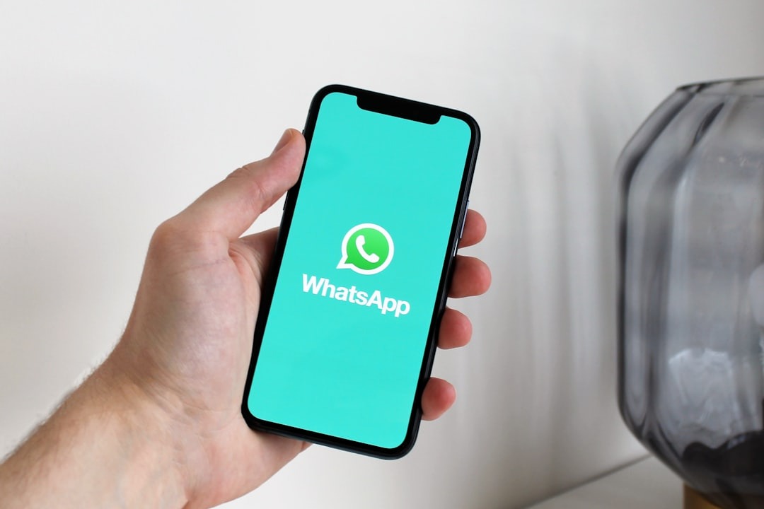 A hand holding a smartphone displaying the WhatsApp logo.